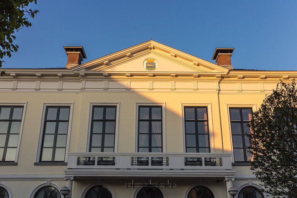 Lichtgele klassieke gevel van het voormalige raadhuis aan de Midstraat in Joure met fronton en wapenschild in avondzon